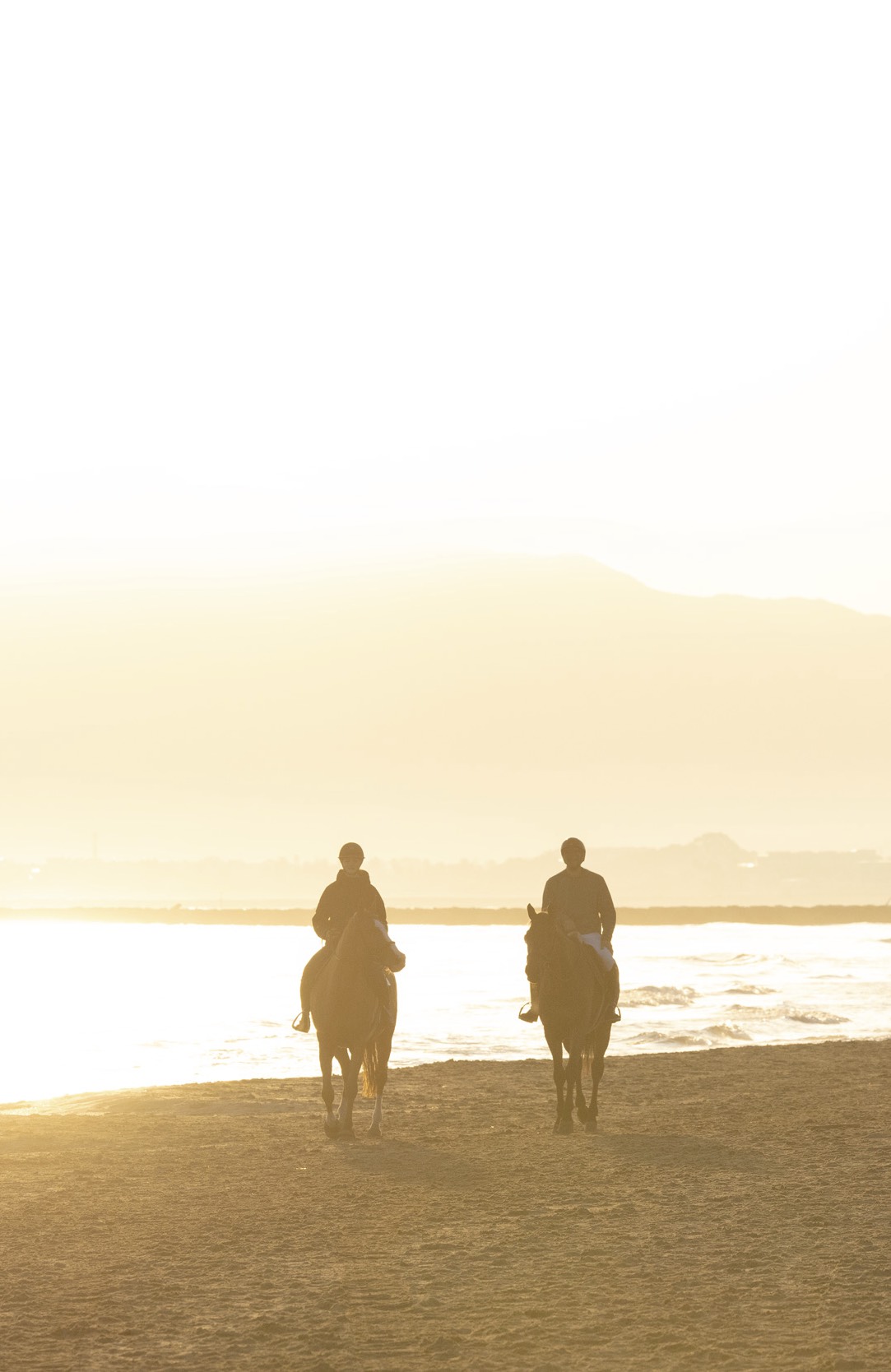 Two riders on horseback at sunset on beach – Risohorse riding surface experience